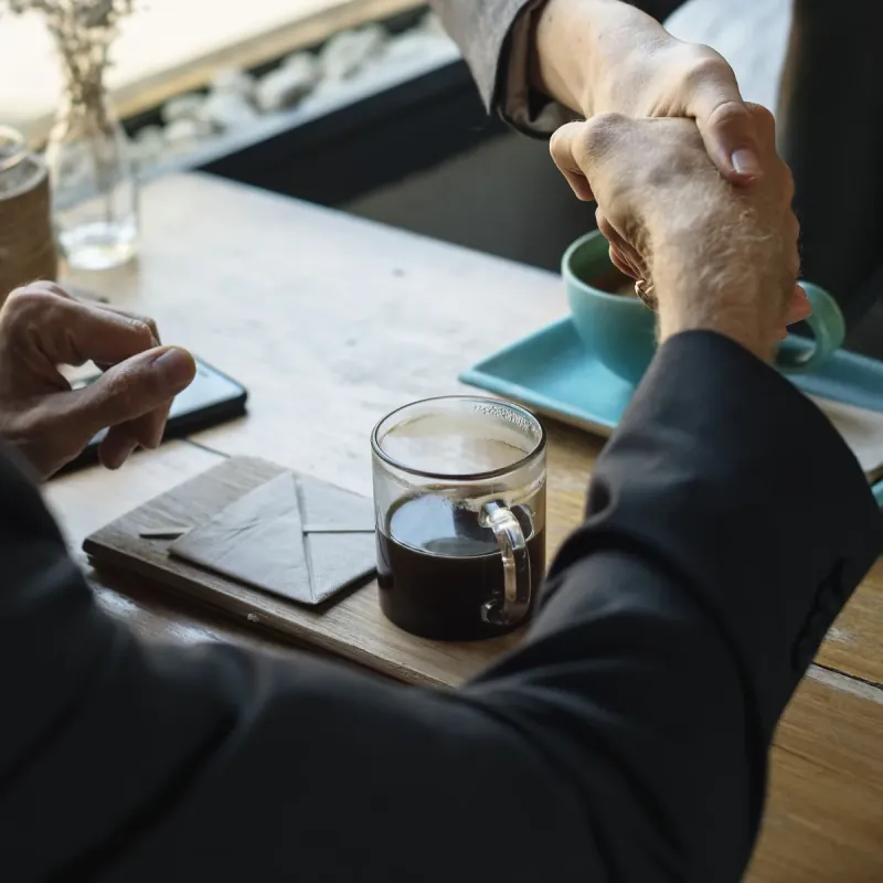 Dos personas se dan la mano sobre la mesa de un café.